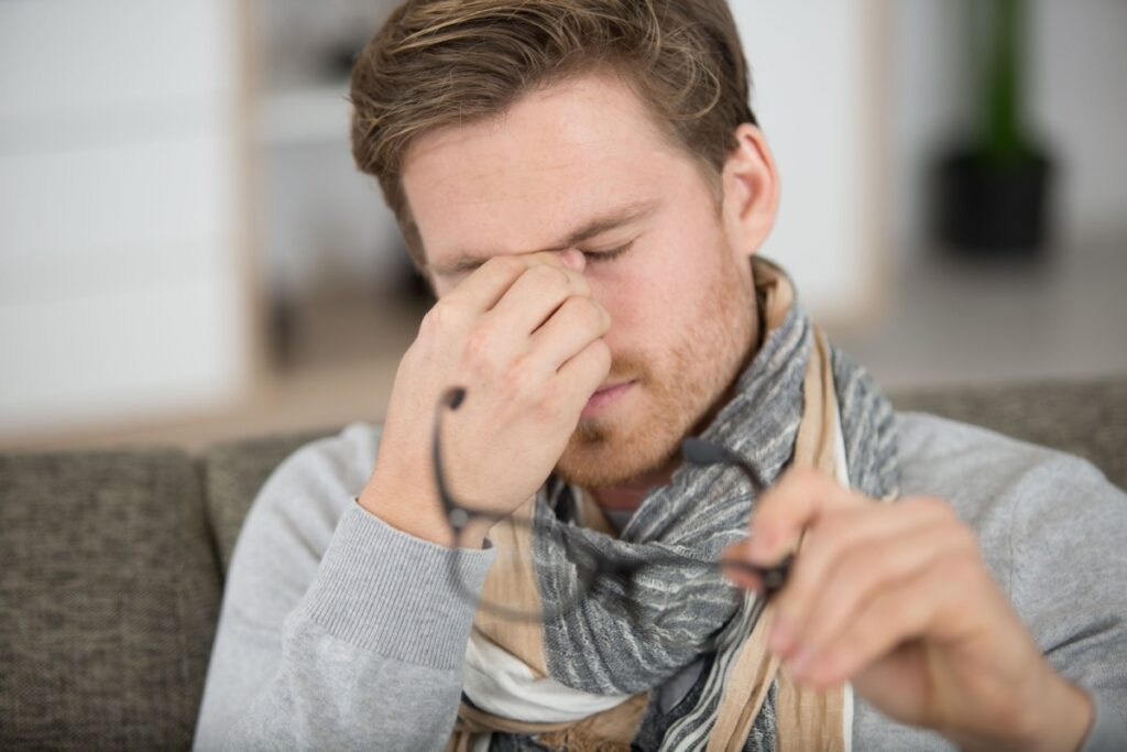 A person removing their glasses to pinch in between their eyes due to irritation caused by dry eye