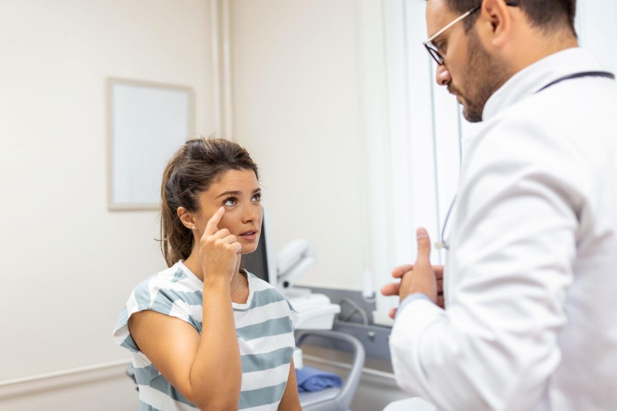 A person pointing to their eye as they talk to an eye doctor