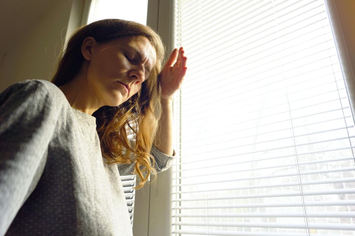 a person holding a hand up and turning their head away from blinds that are open letting bright sun in